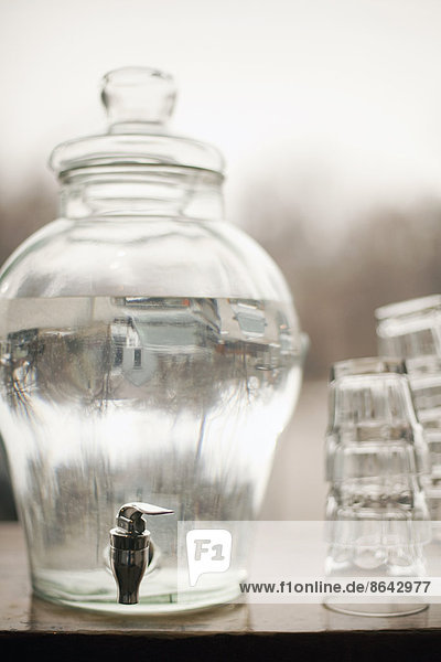 Trinkwasser in einem großen Behälter aus Klarglas. Ein Stapel Gläser. Reines  gekühltes Wasser.
