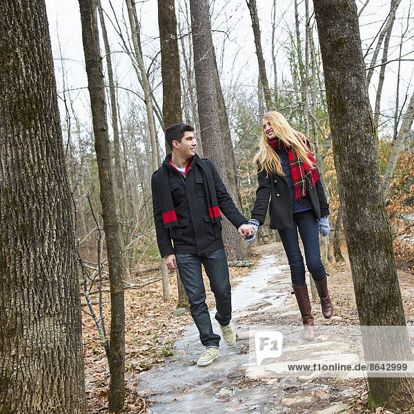 Ein Paar  das im Winter Hand in Hand durch ein Waldgebiet läuft.