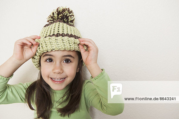 Ein kleines Kind mit langen braunen Haaren das eine Strickmütze mit Pompon trägt und von unten unter der Krempe hervorschaut.