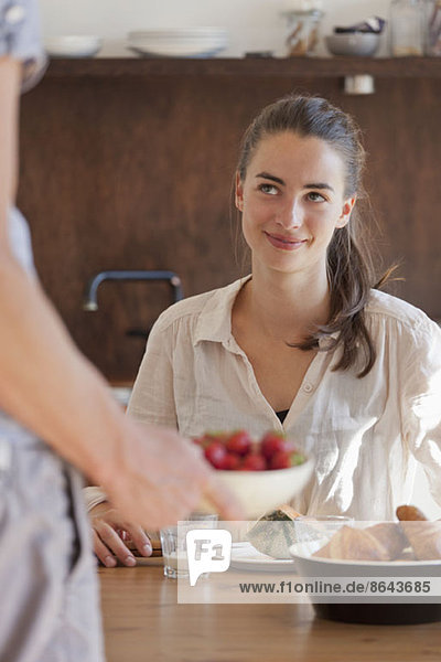 Junge Frau am Esstisch sitzend mit Frühstück  lächelnd