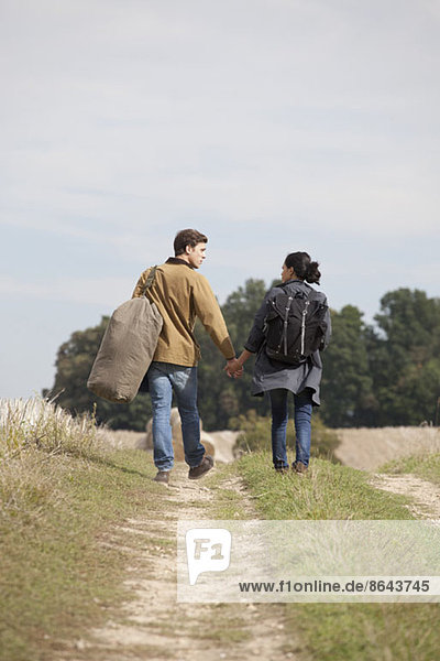 Junges Paar hält sich an den Händen und geht durch den Feldweg.