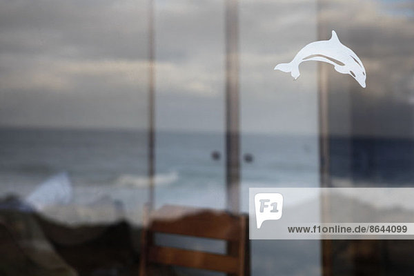 Blick auf das raue Meer durch das Fenster mit Delphinaufkleber