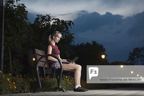 Junge Frau auf Parkbank sitzend und mit Laptop