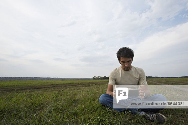 Junger Mann auf Gras sitzend und mit digitalem Tablett