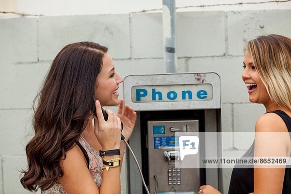 Young women using payphone laughing