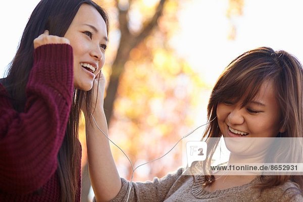 Zwei junge Frauen im Park beim Hören von Kopfhörern