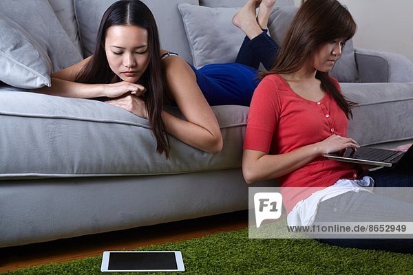 Zwei junge Frauen im Wohnzimmer mit digitalen Tabletten
