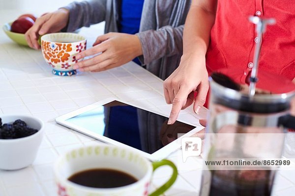 Zwei junge Frauen in der Küche mit digitaler Tablette beim Kaffeetrinken
