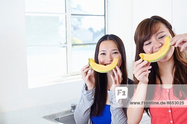 Zwei junge Frauen in der Küche mit Melonen-Smiley-Gesichtern