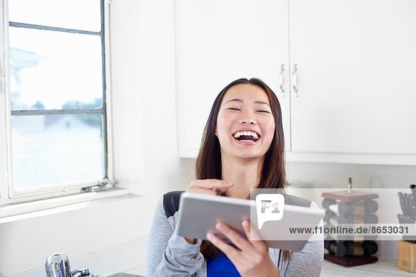 Junge Frau in der Küche lacht über digitales Tablett