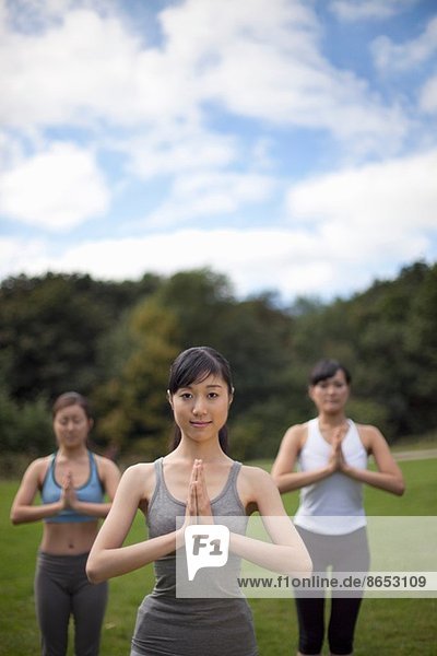 Drei junge Frauen im Park praktizieren Yoga