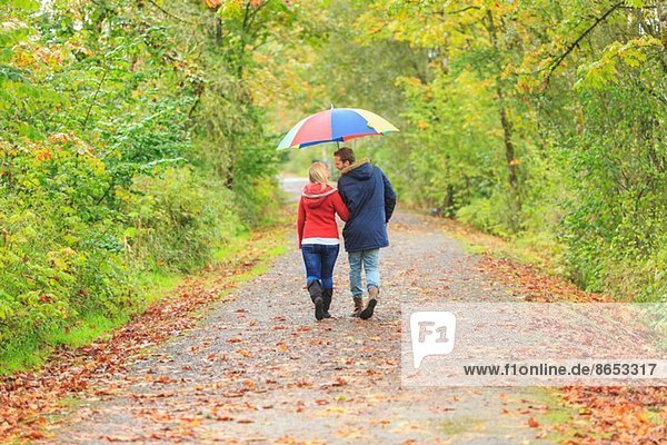 Junges Paar auf dem Landweg mit farbenfrohem Regenschirm