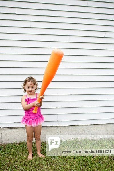 Weibliches Kleinkind im Garten mit einem großen orangenen Baseballschläger