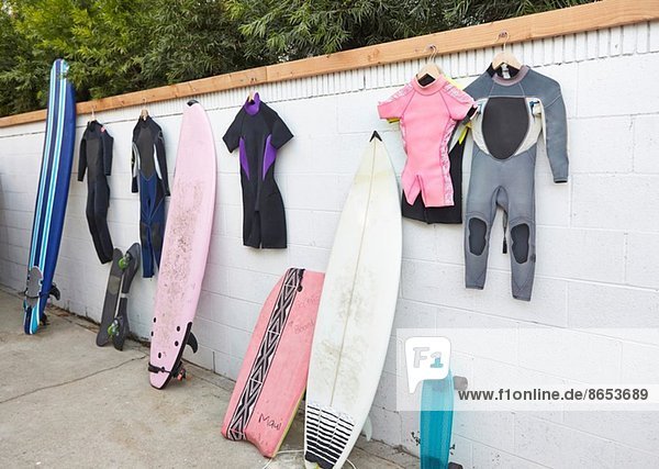 Surfbretter und Skateboards  die sich an die Wand lehnen  und Neoprenanzüge  die an der Wand hängen.