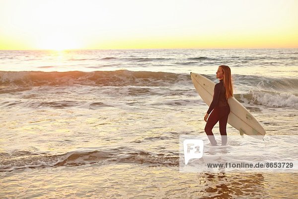 Girl carrying surfboard in sea wearing wetsuit