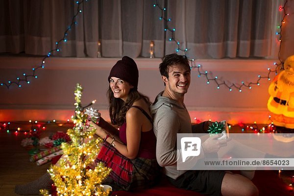 Junges Paar tauscht Geschenke im Wohnzimmer zu Weihnachten aus