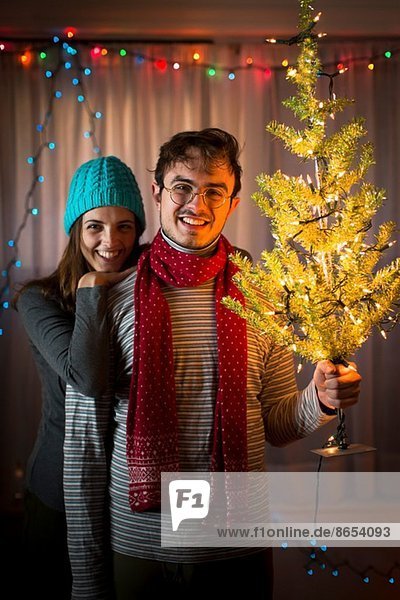 Junges Paar hält beleuchteten Weihnachtsbaum hoch