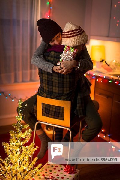 Junges Paar umarmt sich an Weihnachten auf dem Stuhl