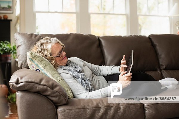Seniorin entspannt auf dem Sofa mit digitalem Tablett