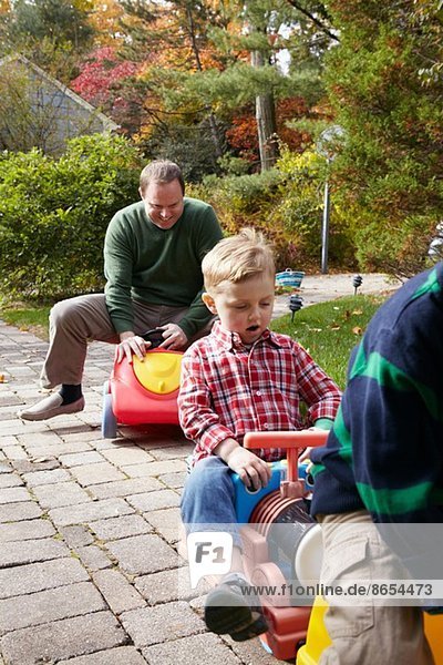 Vater und kleine Söhne beim Spielen auf Spielzeugautos im Garten