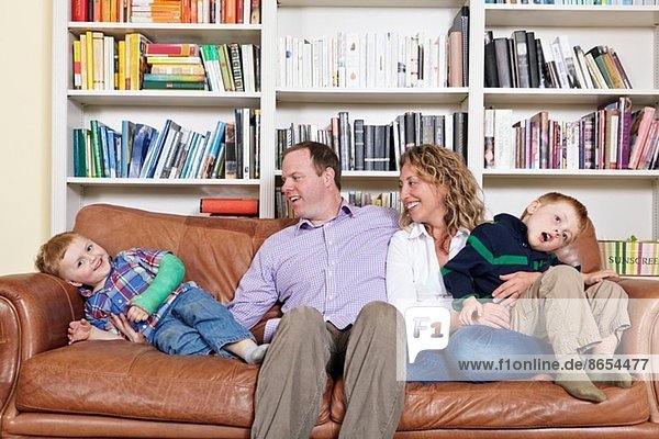 Mid adult parents and young sons having fun on sofa