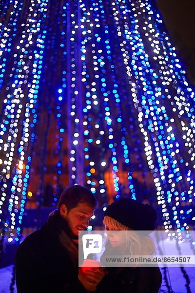 Junges Paar hält Kerze vor Stadt-Weihnachtslicht