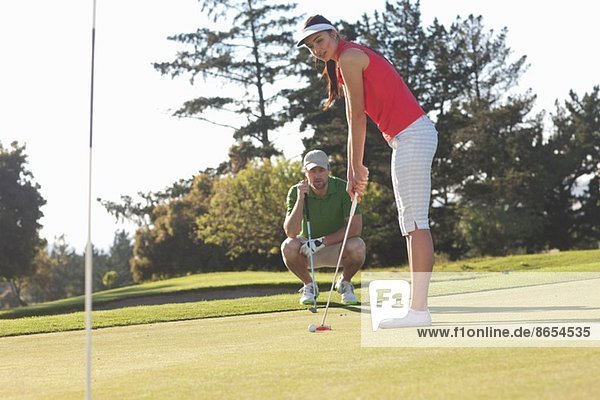 Young female golfer on golf course with trainer