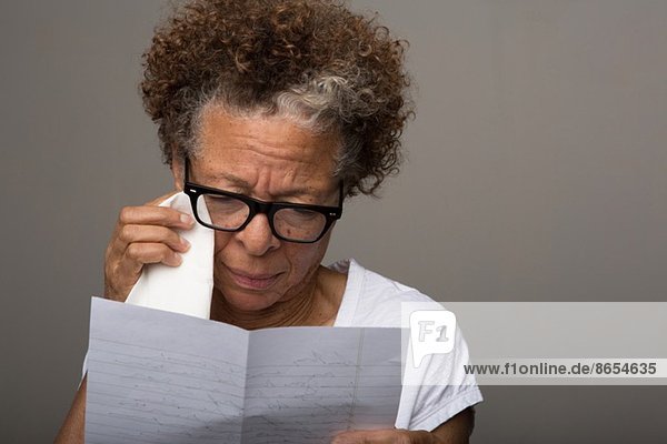 Studio-Porträt einer traurigen Seniorin beim Lesen eines Briefes