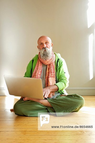 Senior Mann mit Laptop in Lotusstellung