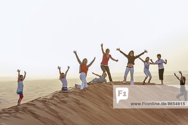 Gruppe von Menschen  die mit erhobenen Armen auf der Wüstendüne stehen.