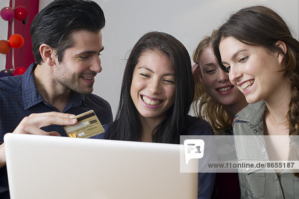 Friends gathered around laptop computer preparing to use credit card for online purchase