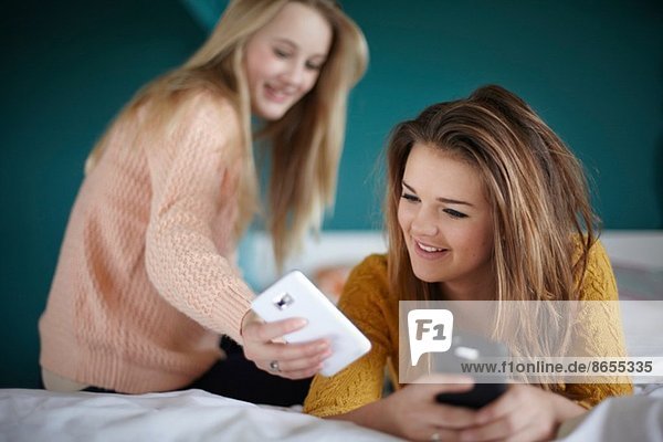 Zwei Teenager-Mädchen  die Smartphones im Schlafzimmer anschauen