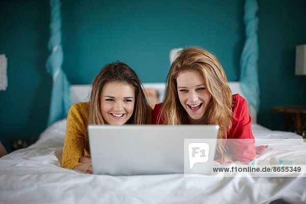 Two teenage girls looking at laptop in bedroom