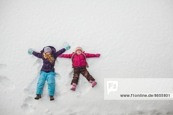 Zwei Schwestern spielen und machen Schnee-Engel im Schnee