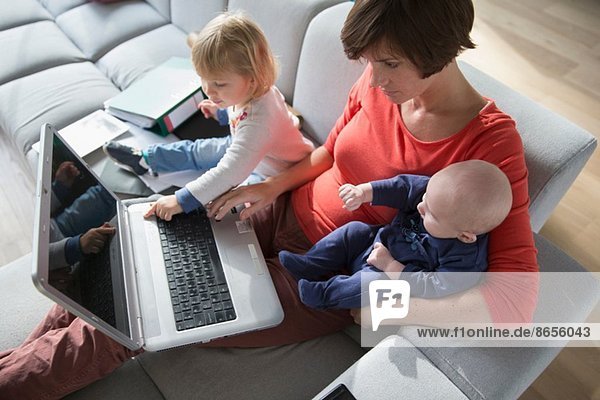 Mother  baby boy and female toddler using laptop on sofa