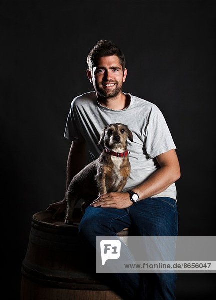 Portrait of winemaker and his dog sitting on wine barrel