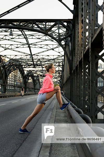 Young female runner stretching legs on bridge