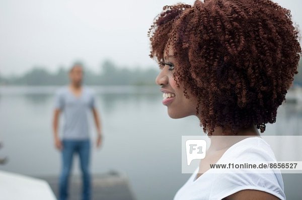 Porträt einer jungen Frau  die mit einem Mann im Hintergrund lächelt.