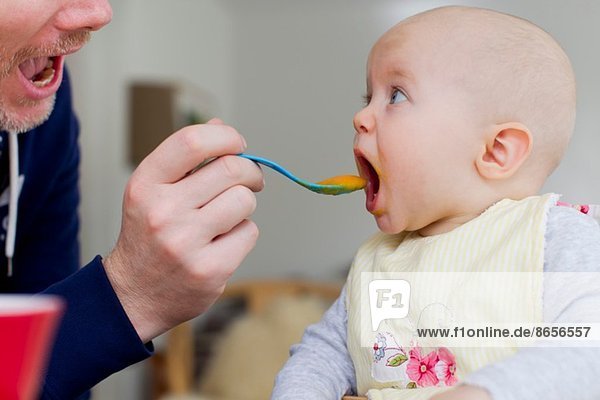 Father spoon feeding baby daughter