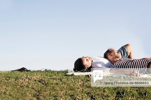 Erwachsenes männliches Paar auf Picknickdecke im Park liegend