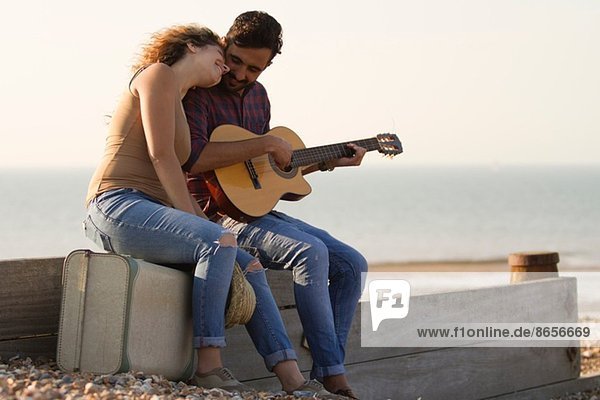 Young couple on beach  man playing guitar