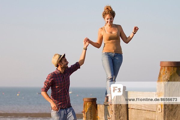 Young woman balancing on groynes holding man's hand