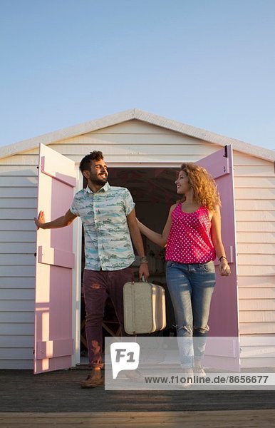 Young couple leaving beach hut with suitcase