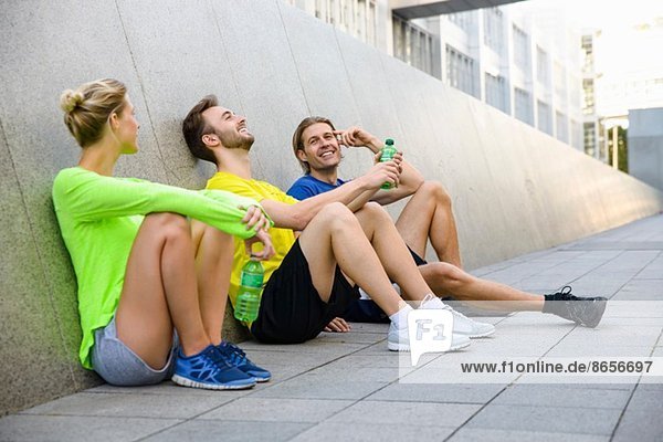 Drei Freunde sitzen auf dem Boden und tragen Sportbekleidung.