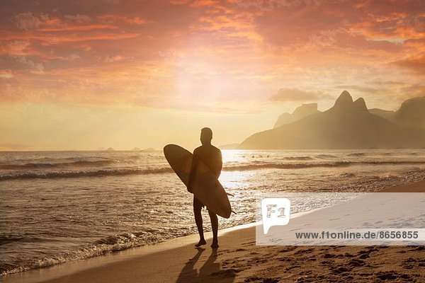 Junger Mann mit Surfbrett am Strand von Ipanema Rio De Janeiro Brasilien