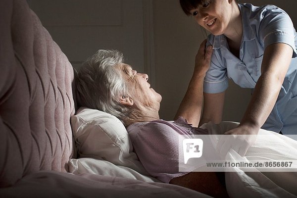 Körperpflege-Assistentin im Gespräch mit Seniorin im Bett