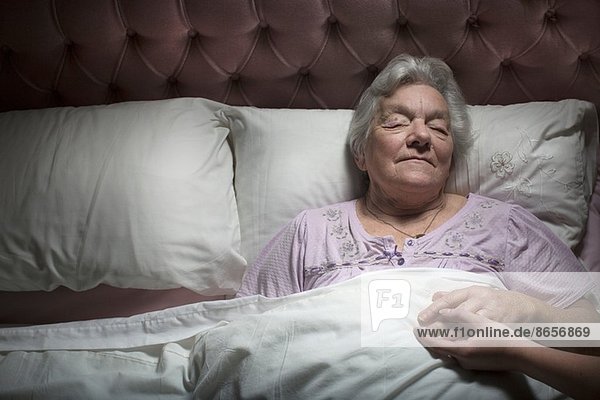 Junge Frau hält die Hand der schlafenden Seniorin.