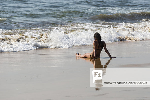 A young woman wearing bikini is sitting in the sand of Anjuna Beach  Anjuna  Goa  India