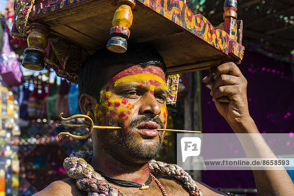 Mann mit einem kleinen Messingdreizack  der seine Wange durchstößt  sammelt Geld für religiöse Zwecke  auf dem wöchentlichen Flohmarkt  Anjuna  Goa  Indien