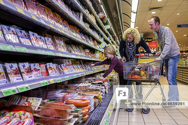 Family shopping with a shopping trolley in the refrigerated section of a supermarket with packed meat  Germany
